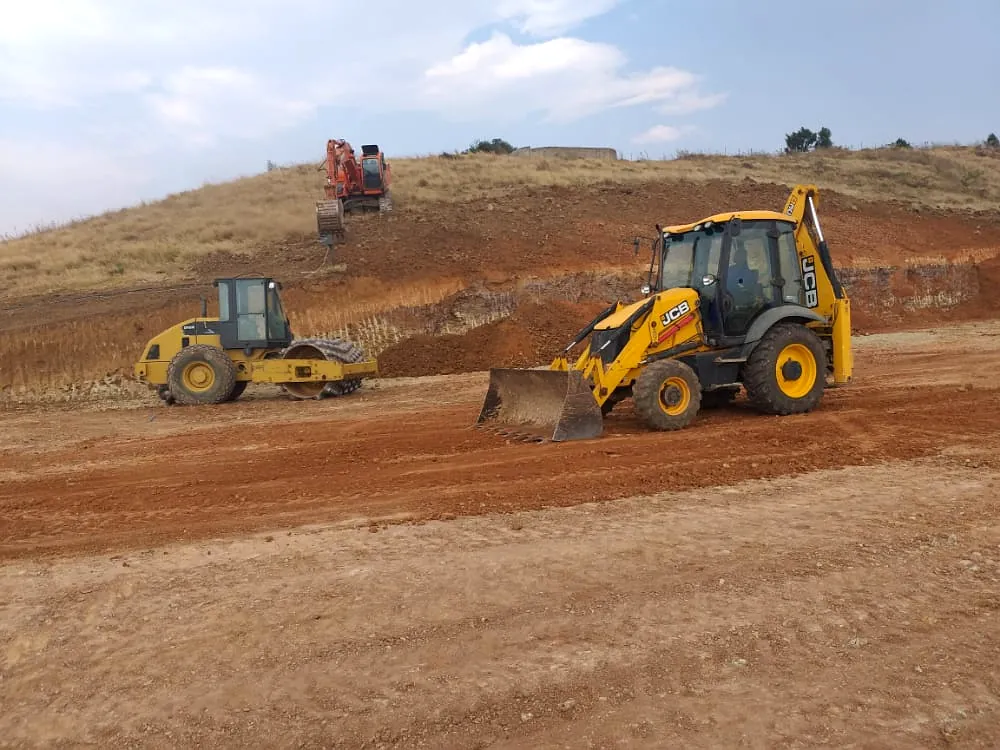 Roller and loader grading a building platform during site establishment