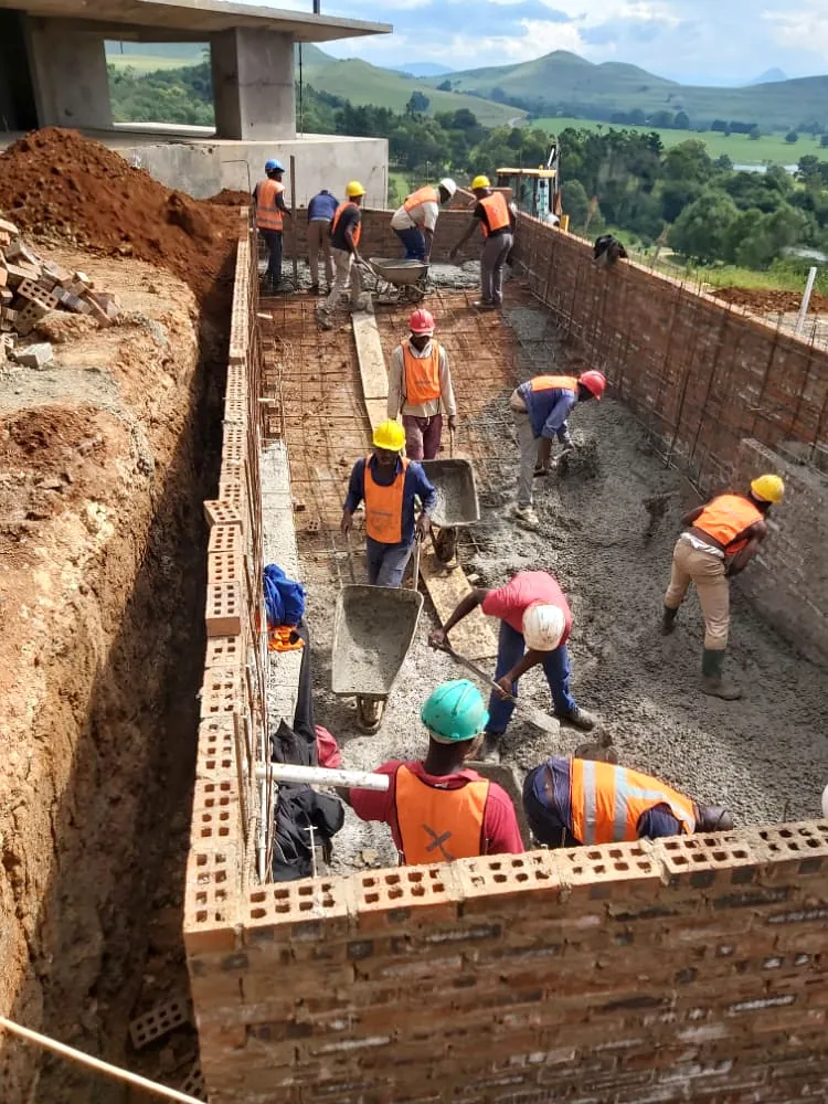 Construction team laying brickwork to foundations in an excavated trench